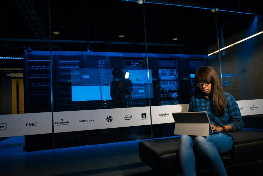Woman using a laptop in a server room, showcasing modern technology and work environment.