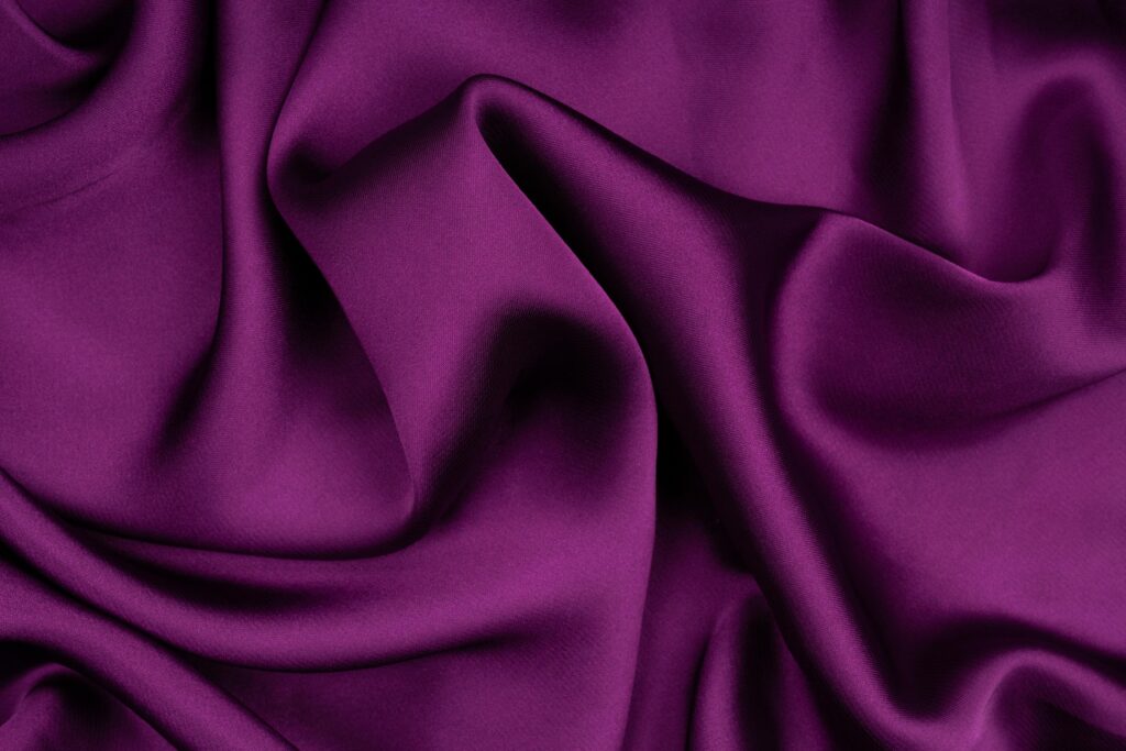 A detailed close-up of luxurious purple silk fabric with elegant folds and smooth texture.