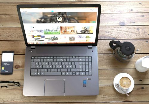 Top view of a laptop, smartphone, coffee, and glasses on a wooden desk.